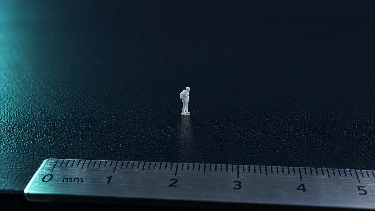 Figura minúscula impressa em 3D no meio de uma mesa de impressora vazia, com régua em milímetros